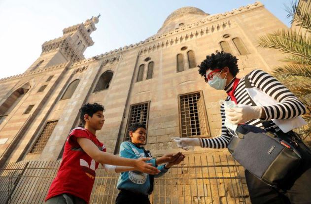 الطالب أحمد ناصر يرش الكحول المعقم على أيدي طفلين في حي القلعة بوسط القاهرة في صورة بتاريخ 13 ابريل 2020. تصوير: محمد عبد الغني - رويترز.